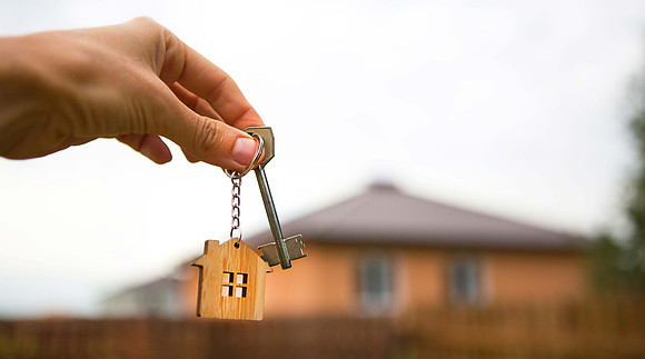Hand,With,A,Key,And,A,Wooden,Key,Ring-house.,Background
